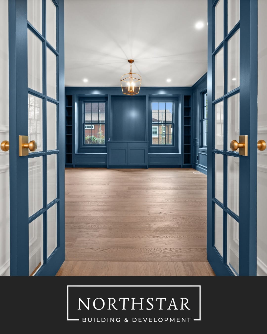 Blue paneled home office with glass doors and built-in shelves shared by North Star Builders